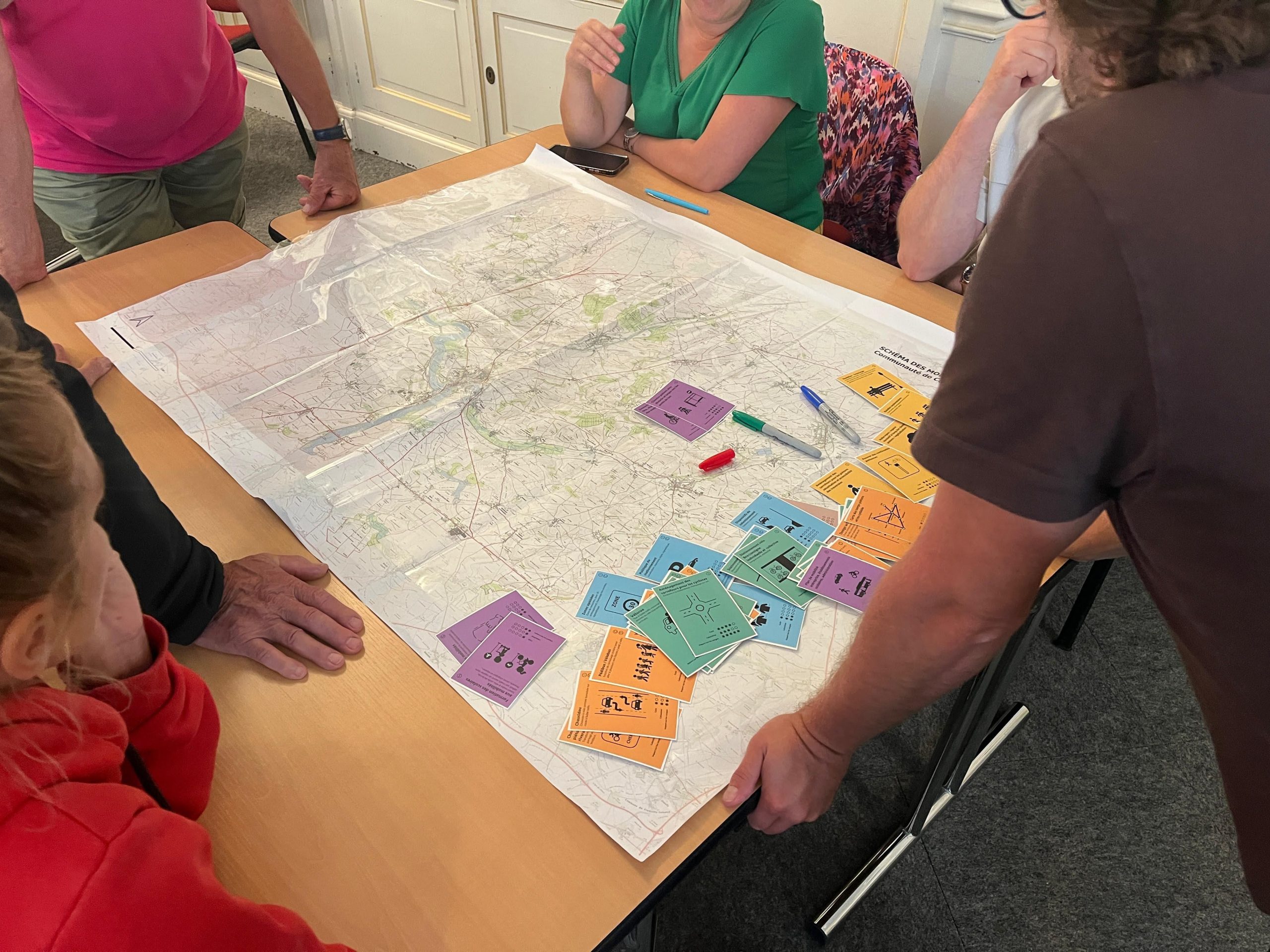 Participants réunis autour d'une grande carte du territoire lors d'un atelier de concertation, avec des cartes-actions de couleur posées sur le plan et des feutres.