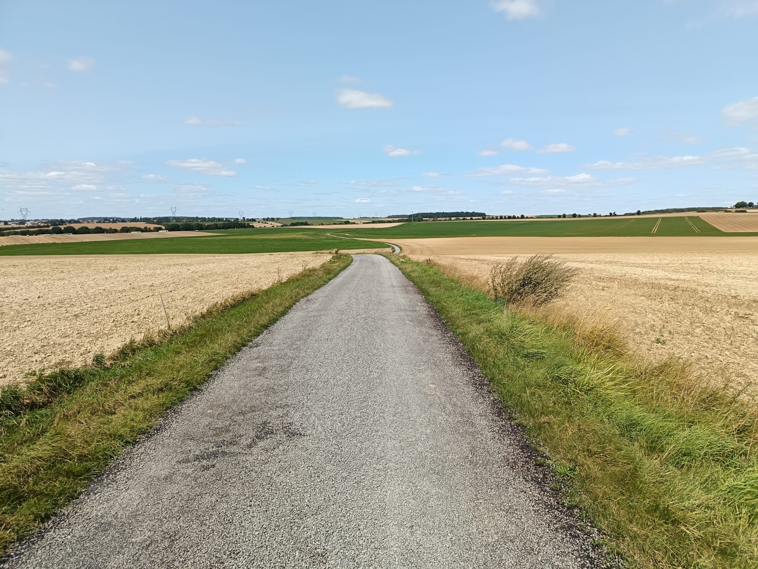 Route de campagne étroite et sans marquage traversant un plateau agricole de la Haute Somme.