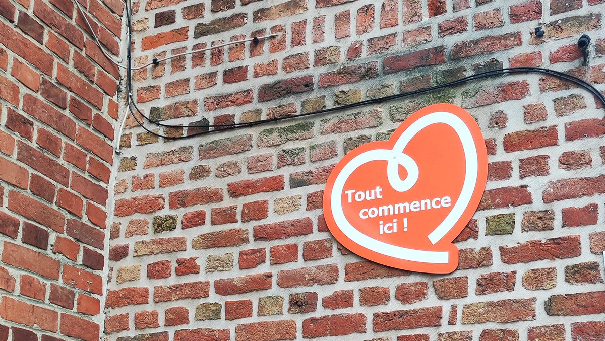 Support d'invitation en forme de coeur accompagné du texte "Tout commence ici !" sur le mur de la médiathèque d'Haverskerque